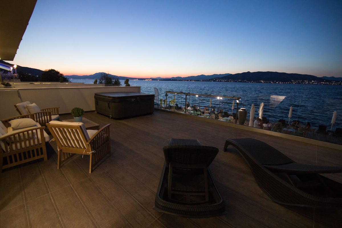 Una terraza con mobiliario de mimbre, una mesita y vistas al agua y montañas a lo lejos.