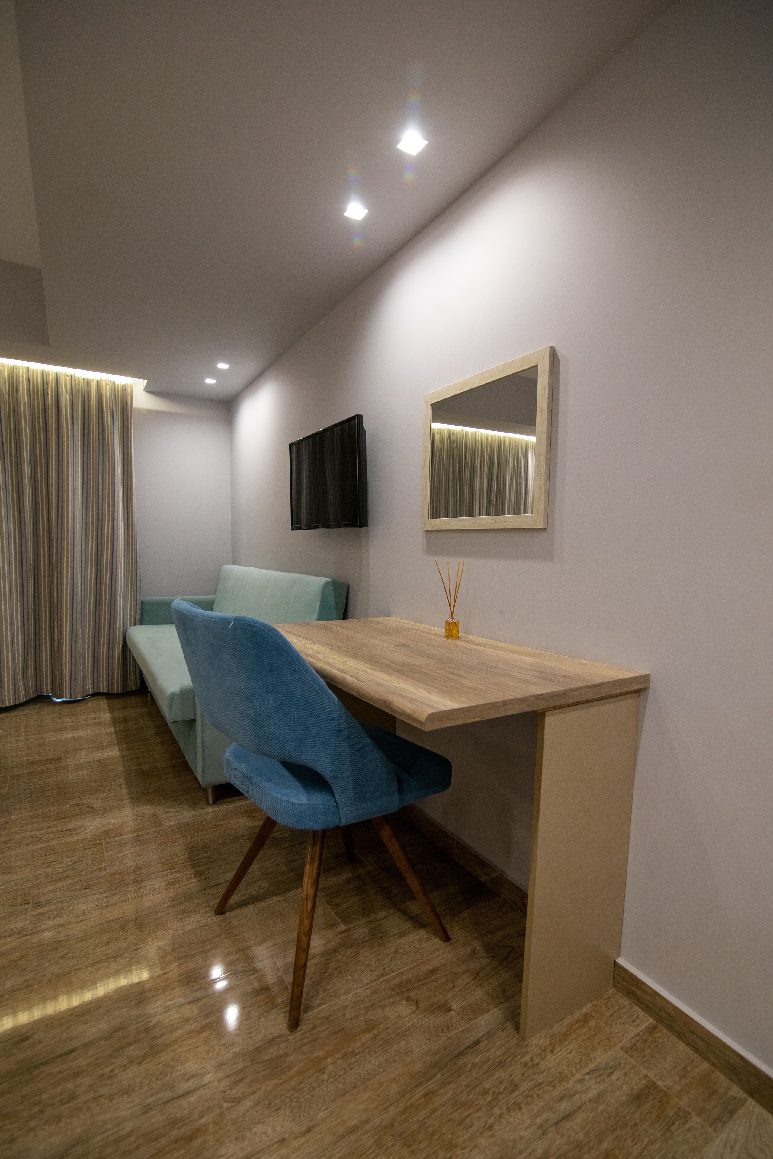 A modern room with a wooden desk, a blue chair, a light blue sofa, a flat-screen TV, and a mirror on the wall.