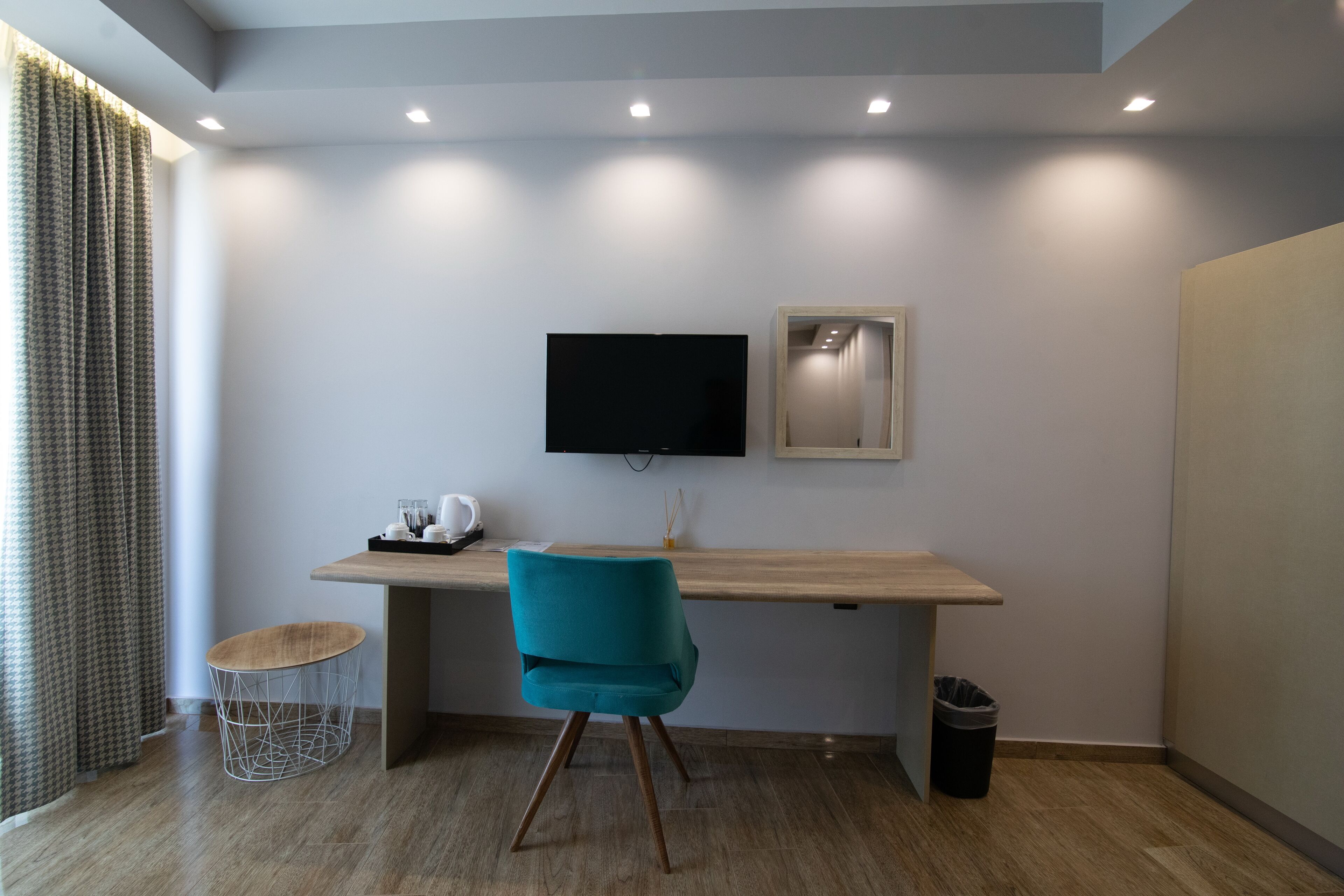A modern room with a wooden desk, a teal chair, a television, and a mirror on the wall.