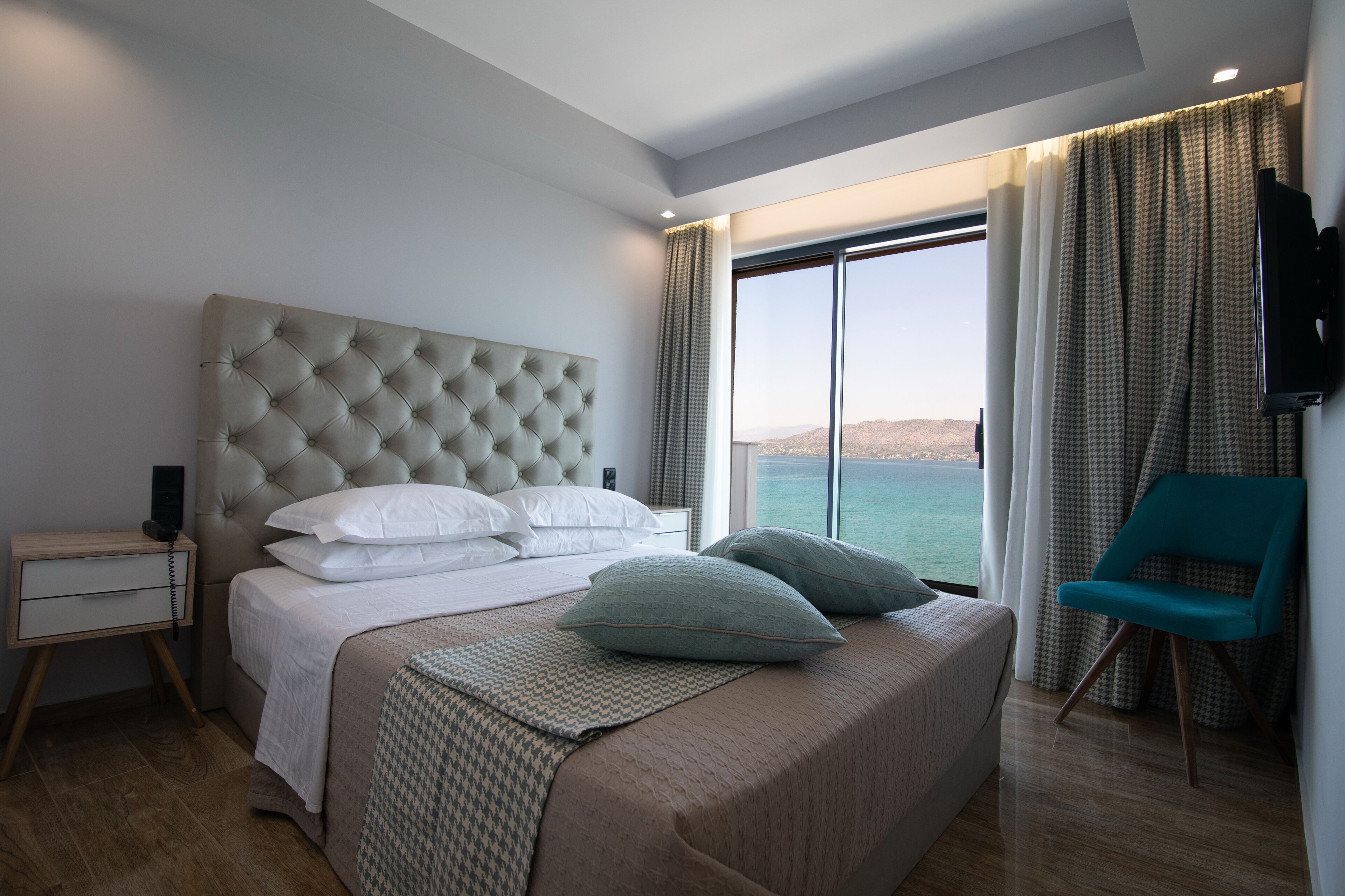 Une chambre à coucher moderne avec un grand lit, une table de chevet, une chaise et une vue sur la mer.