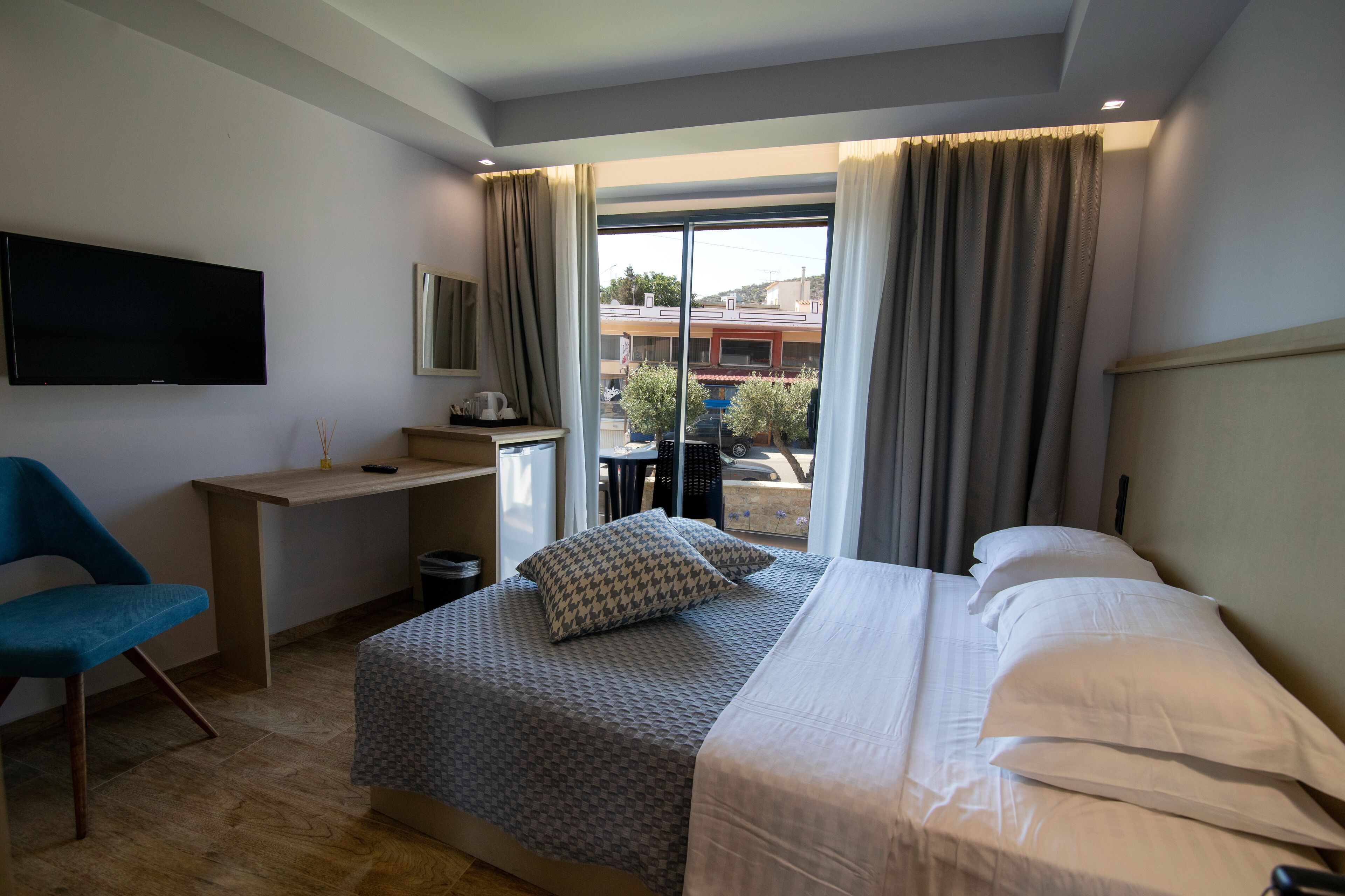 Habitación de hotel con cama, escritorio, silla, televisión y ventana con cortinas.
