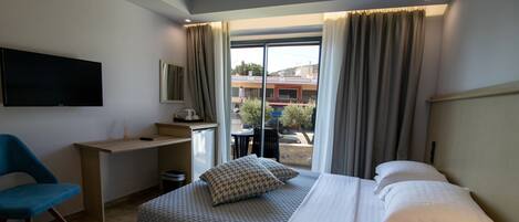 Habitación de hotel con cama, escritorio, silla, televisión y ventana con cortinas.