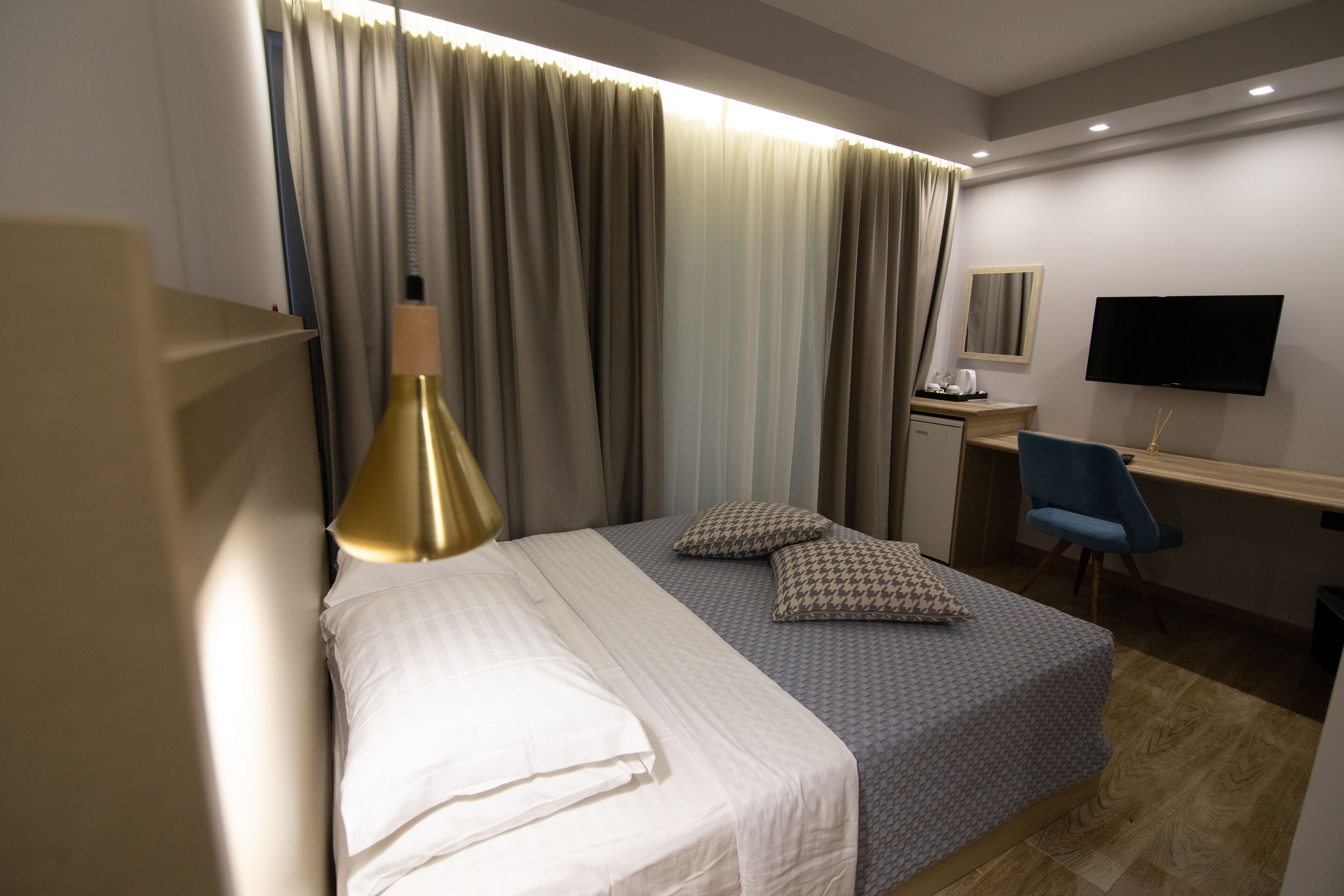 Habitación de hotel con cama, cortinas, escritorio con silla, televisor y lámpara.