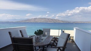 Une terrasse dotée de mobilier en bois et offrant une vue sur la mer et les montagnes.