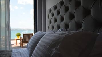 A bedroom with a large bed, a tufted headboard, a view of the sea, and a balcony with a chair and a plant.
