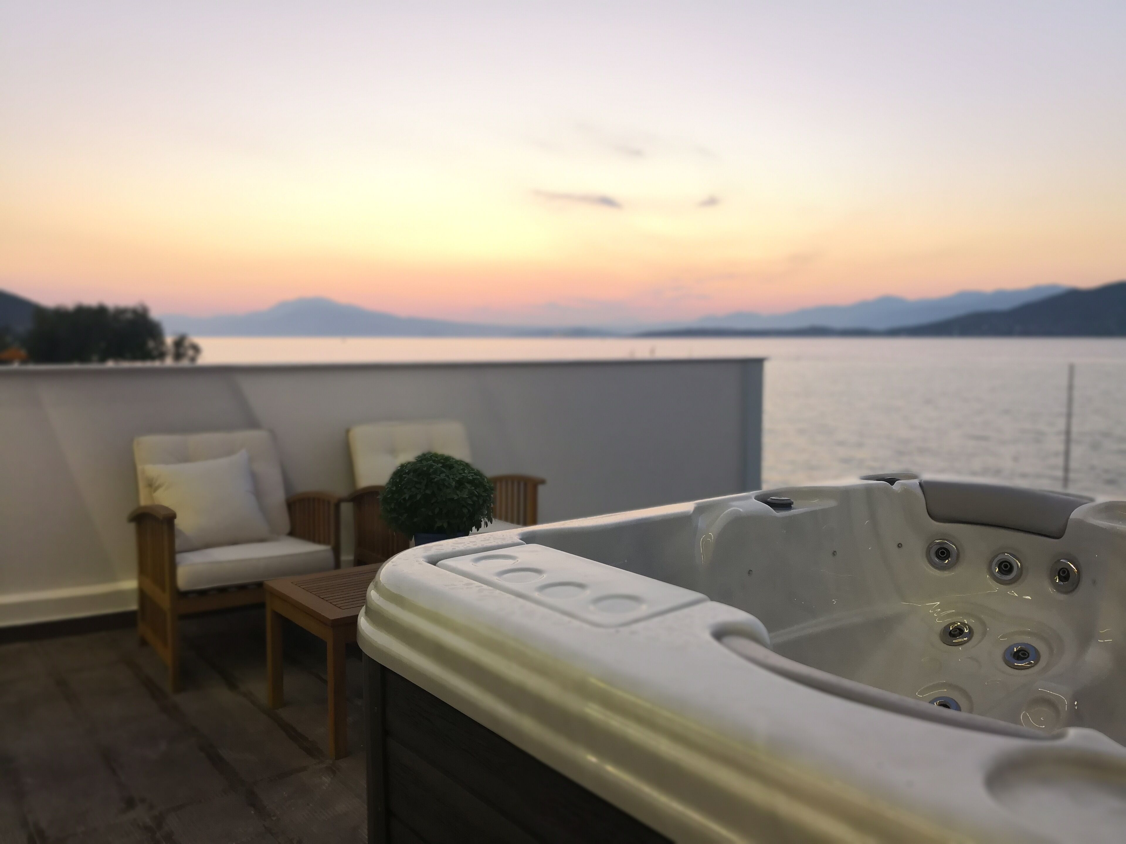 Un jacuzzi en un balcón con vistas a un lago y montañas al atardecer.