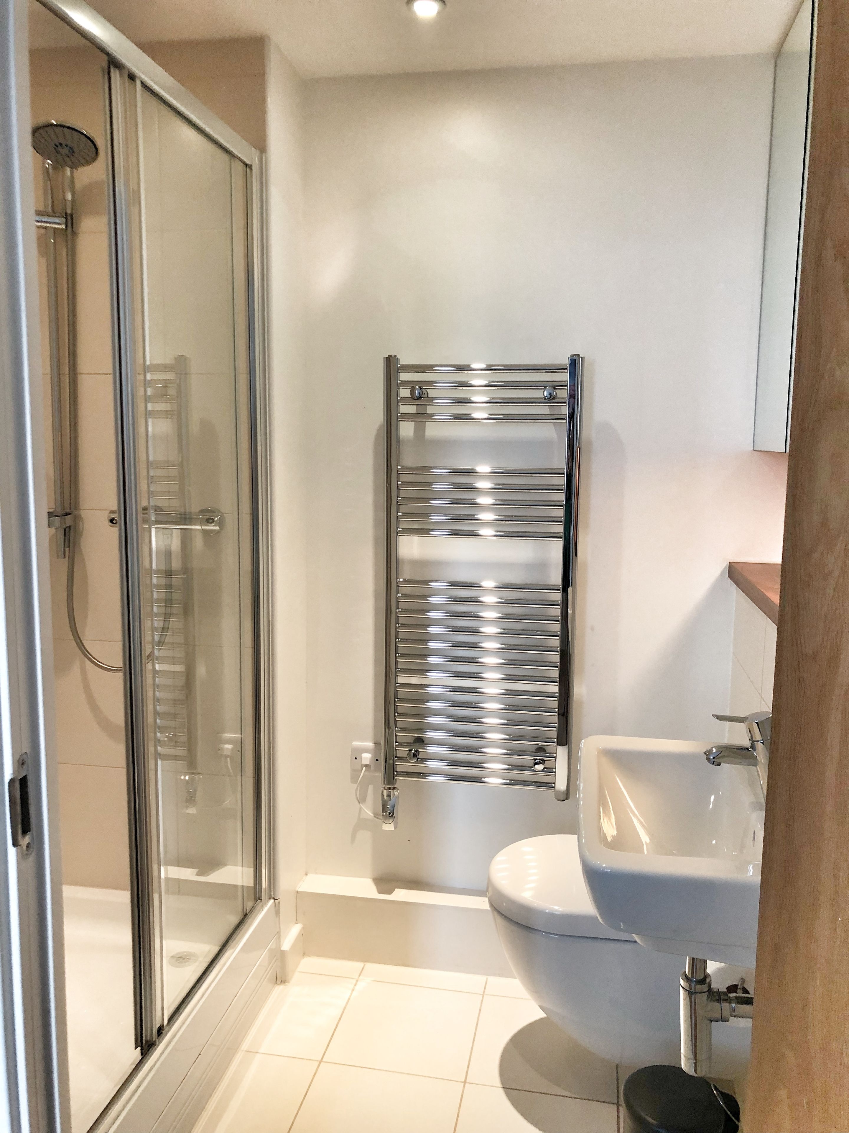 Un baño moderno con cabina de ducha de vidrio, toallero cromado y lavamanos blanco.