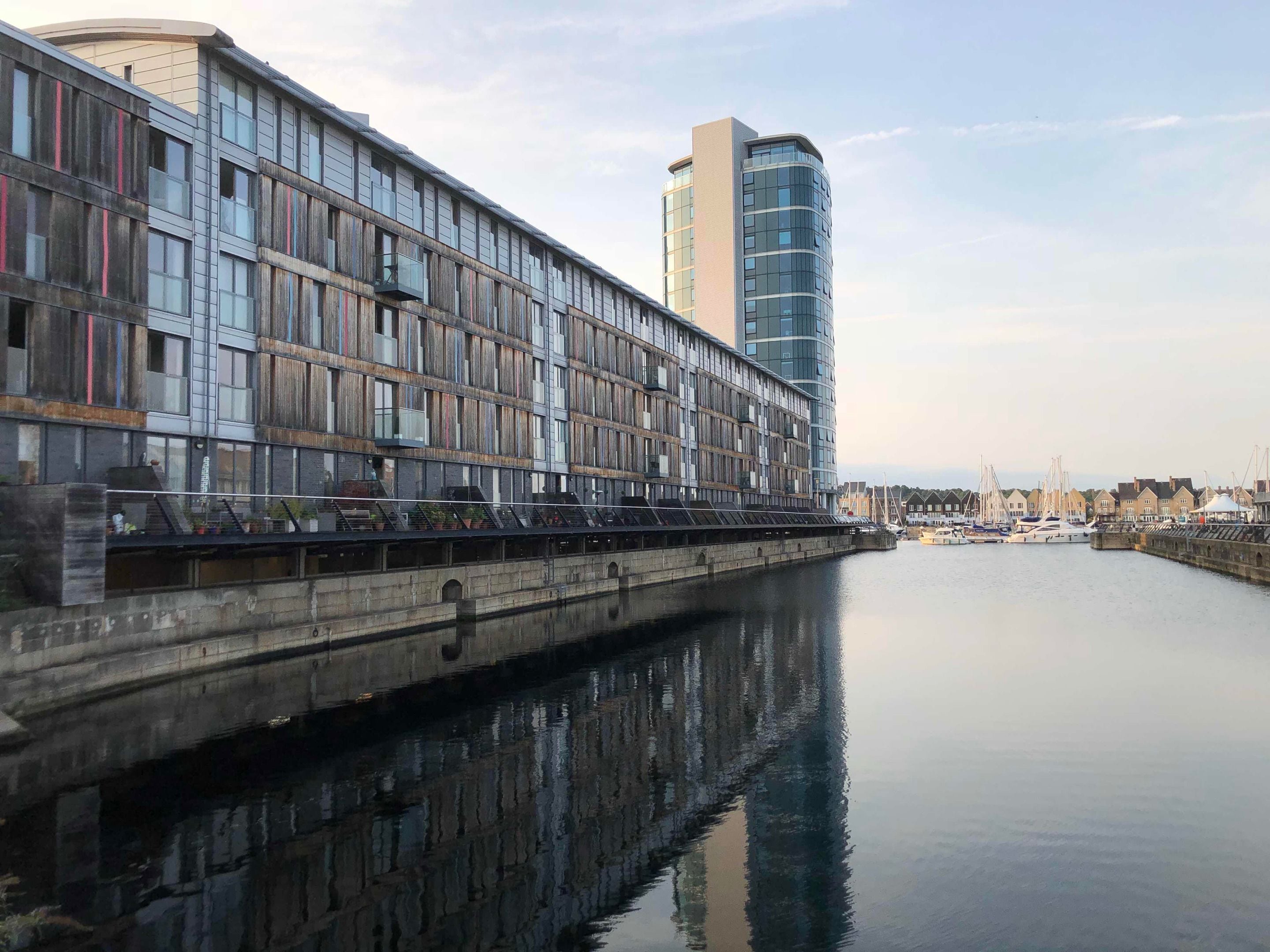 Um edifício moderno à beira-mar, com grandes janelas e superfície aquática refletora.