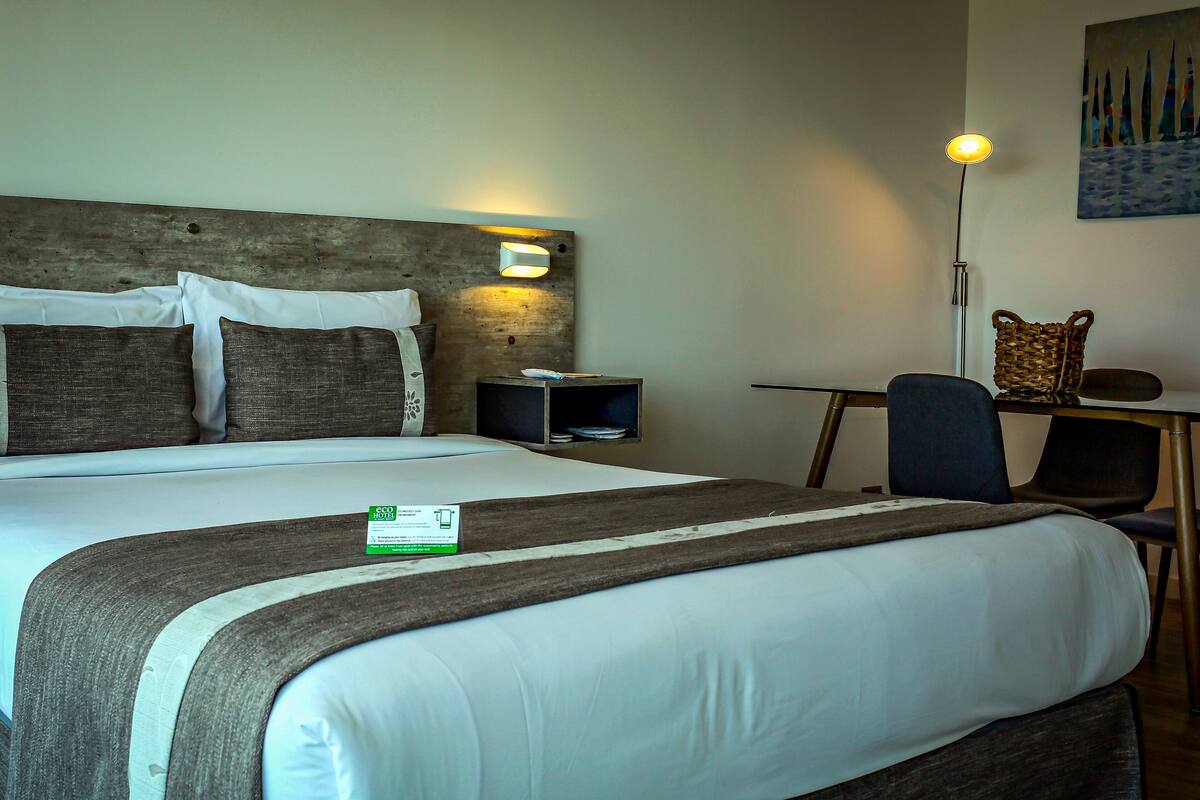 A hotel room with a large bed, a wooden headboard, a nightstand, a desk, and a chair.