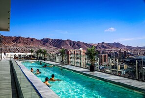 A rooftop pool with clear blue water, surrounded by mountains and a cityscape. - EcoApart Antofagasta (Antofagasta)