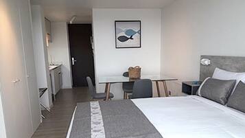 A hotel room with a bed, a desk, a chair, and a door.