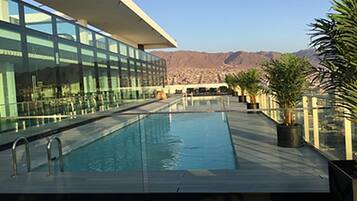 Una piscina con un edificio moderno al fondo y montañas a lo lejos.