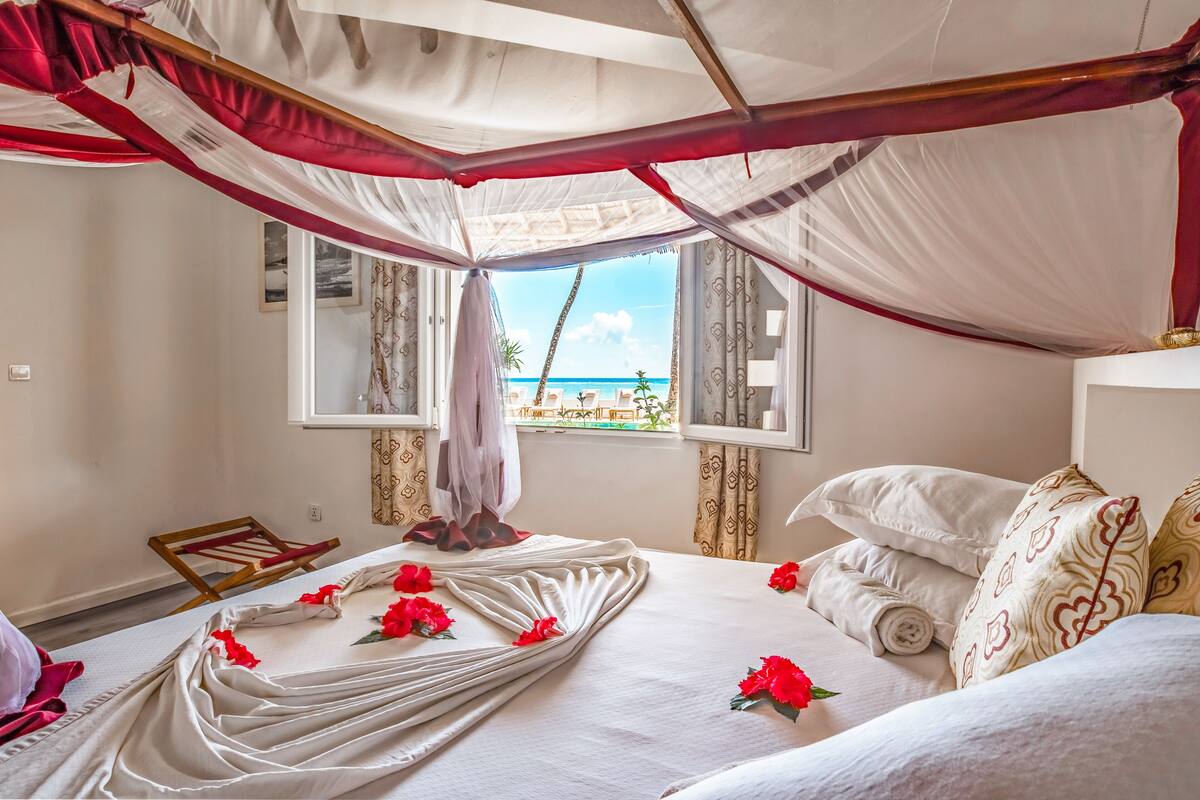 Une chambre avec un lit, une fenêtre donnant sur la plage et un couvre-lit à baldaquin.