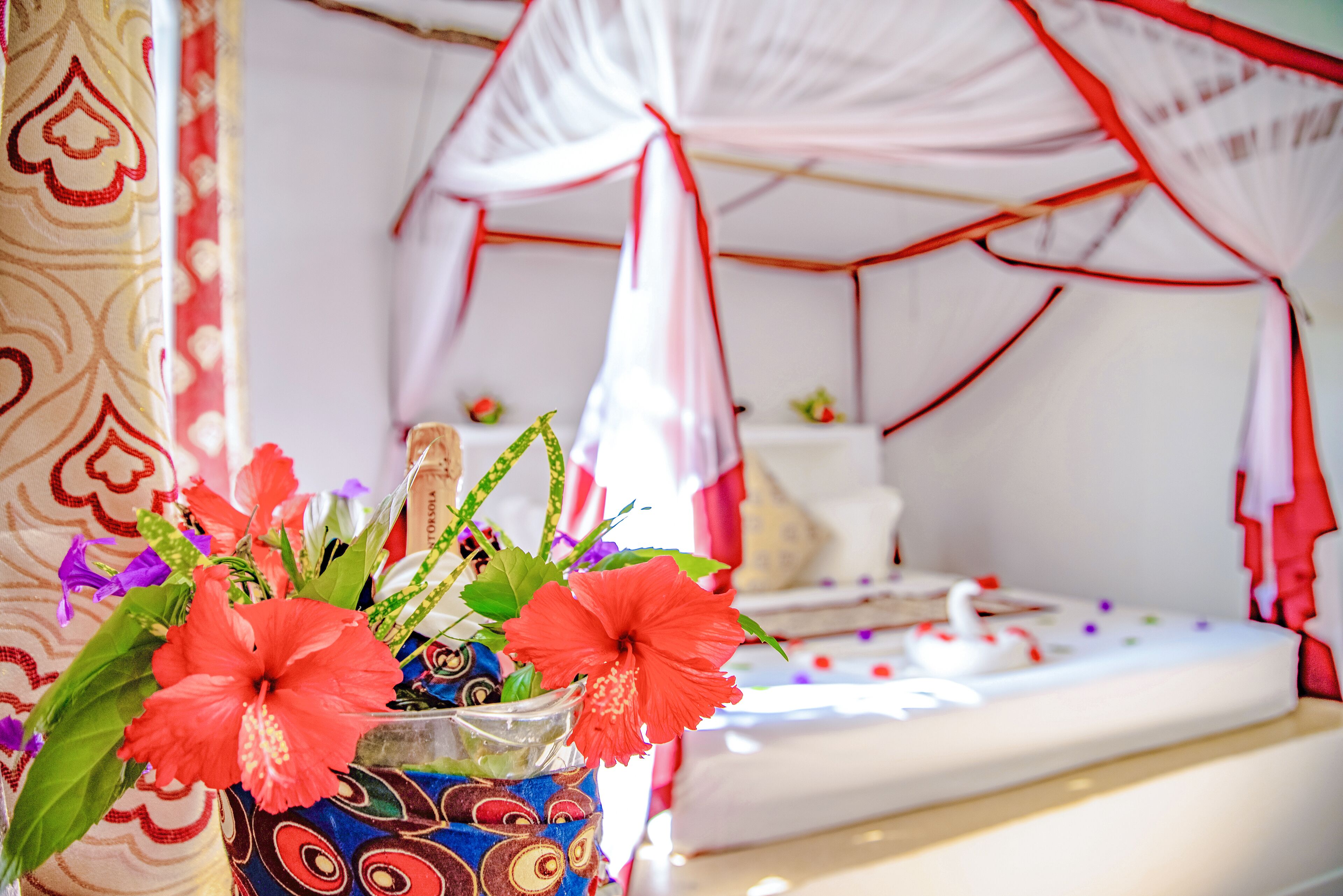 A bed with a canopy, a vase with flowers, and a patterned wall.