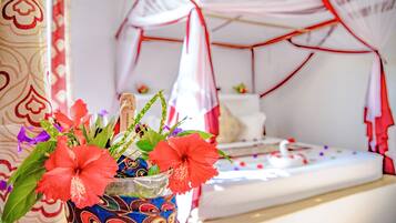 A bed with a canopy, a vase with flowers, and a patterned wall.