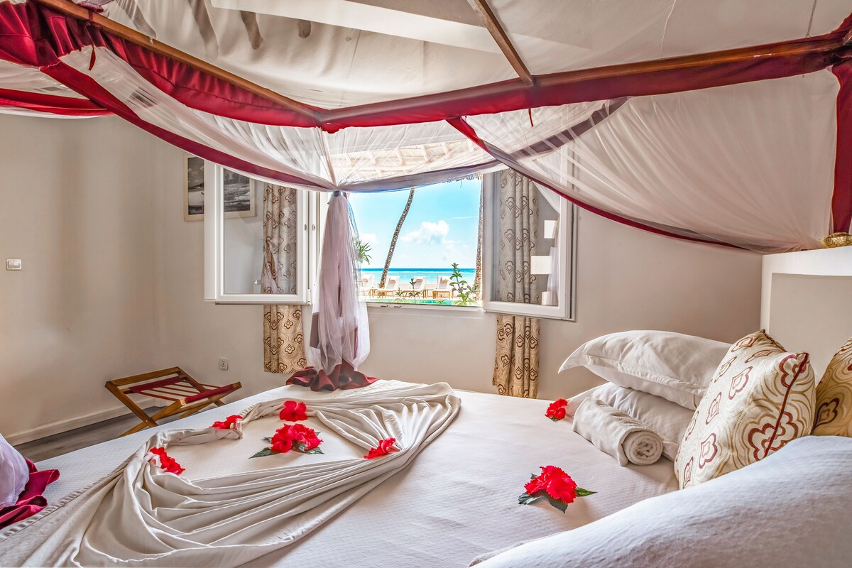 Ein Zimmer mit einem Bett, einem Fenster mit Blick auf den Strand und einem Baldachin.