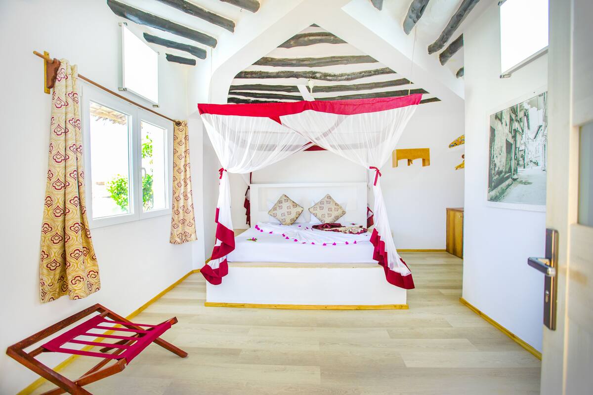 Une chambre avec un lit sous un dais, une chaise en bois et un tableau accroché au mur.
