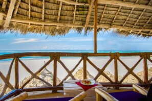 Blick auf einen Strand von einer Holzterrasse mit einem Reetdach, mit Blick auf den Ozean.