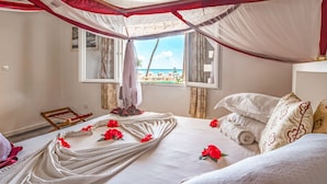 Een kamer met een bed, een raam met uitzicht op het strand en een hemelbedspreider.
