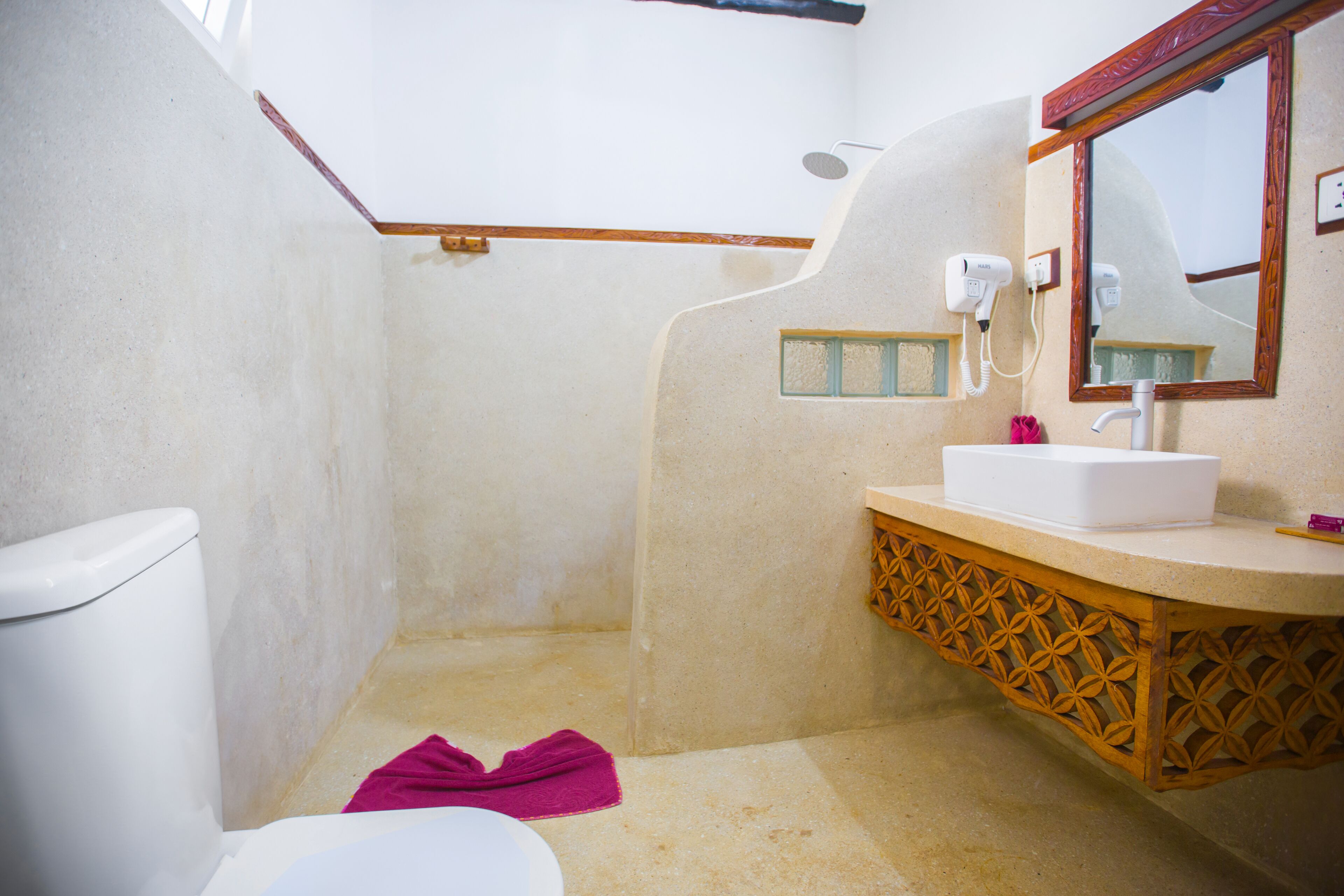 A bathroom with a white toilet, a sink with a wooden vanity, a shower area, and a mirror with a wooden frame.