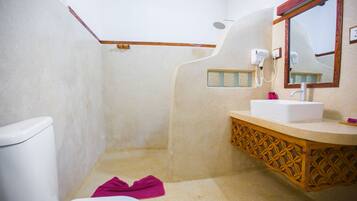 A bathroom with a white toilet, a sink with a wooden vanity, a shower area, and a mirror with a wooden frame.