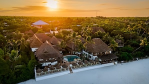 Een resort met rieten gebouwen, een zwembad en palmbomen.