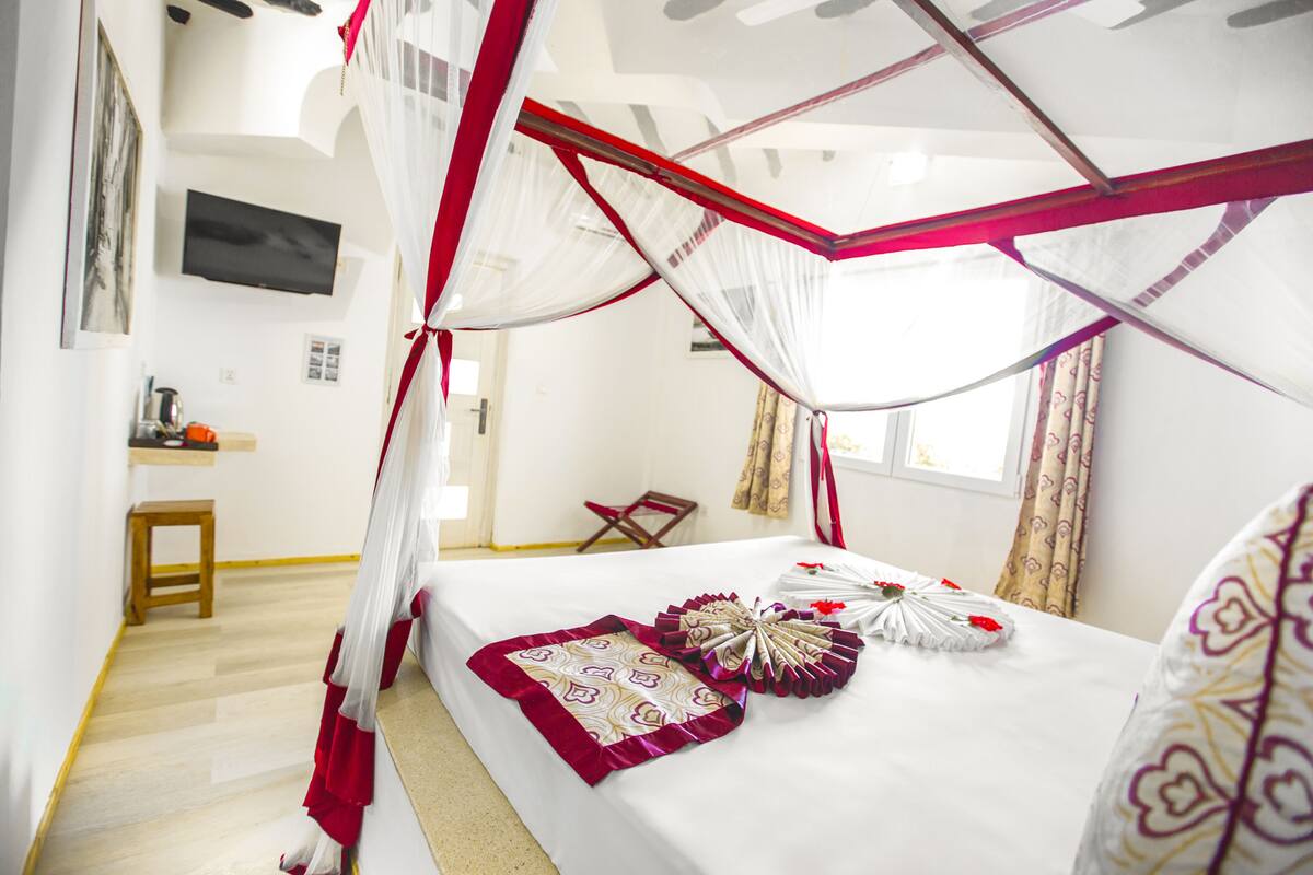 Une chambre à coucher avec un lit à baldaquin, une table de chevet, une chaise et un téléviseur fixé au mur.