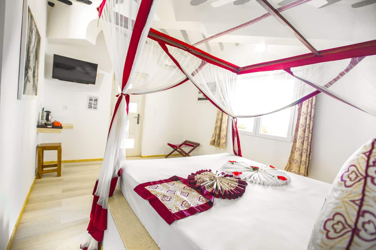 A bedroom with a canopy bed, a bedside table, a chair, and a television on the wall.