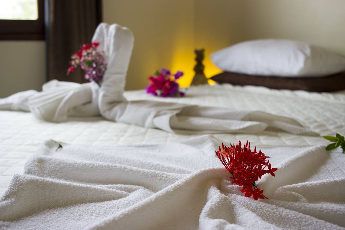 A neatly made bed with white linens and a red flower on the bedspread.