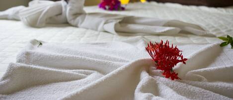 A neatly made bed with white linens and a red flower on the bedspread.