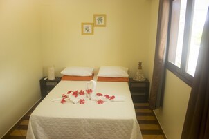 A hotel room with a bed, two pillows, a nightstand, a vase, and a window with curtains.