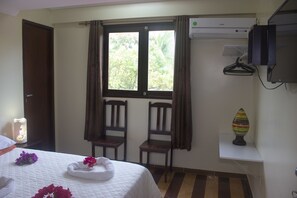 Relax in a serene space with a comfortable bed, two chairs by the window, and a TV for entertainment.