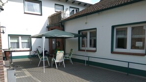 Een terras buiten met een tafel, stoelen, een fiets en een gebouw met ramen en een balkon.