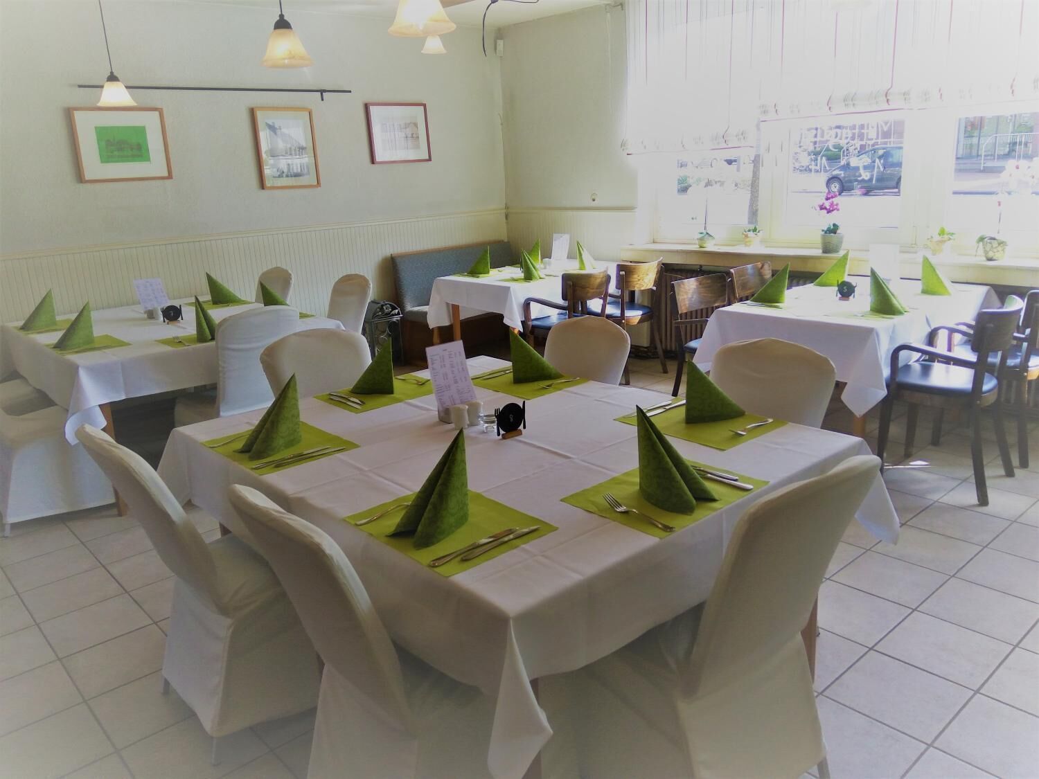 A restaurant with white tablecloths, green napkin cones, and white chairs.