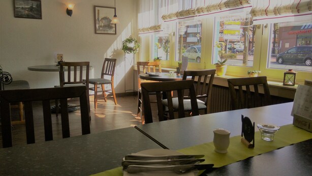 Een restaurantinterieur met houten tafels en stoelen, foto's in lijsten aan de muur en grote ramen met uitzicht op de straat.