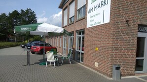 Een bakstenen gebouw met een bord waarop 'Castillo AM Markt' staat, en terrasstoelen met parasols.