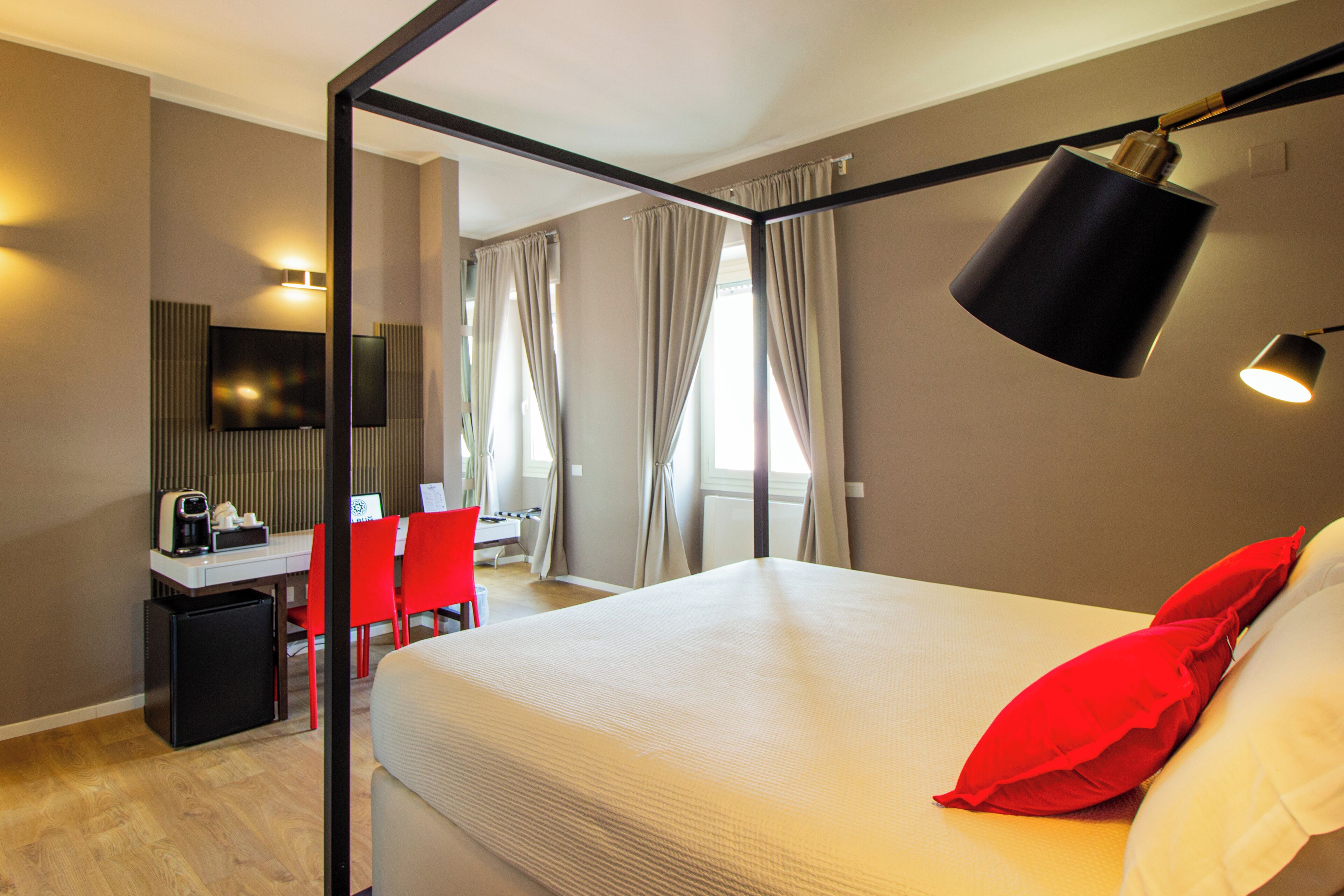 A hotel room with a bed, a desk with a computer, a chair, and a small refrigerator.