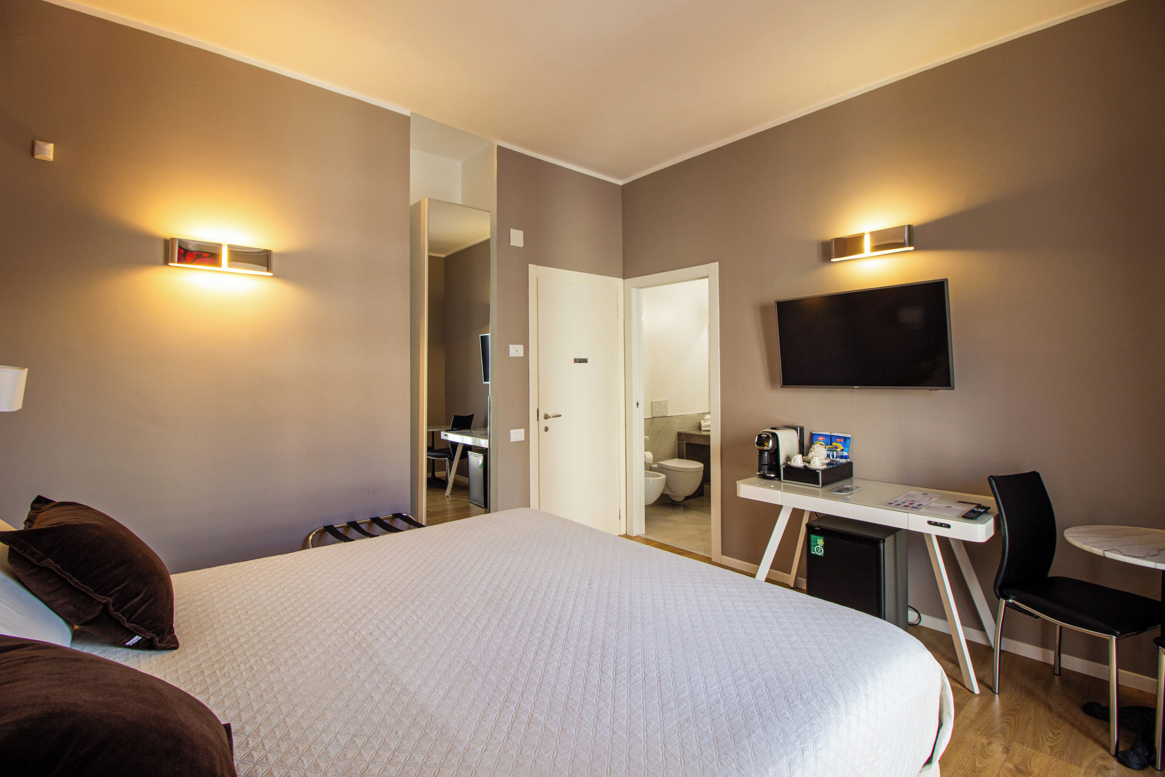 A hotel room with a large bed, a desk with a chair, a television, and a small table.