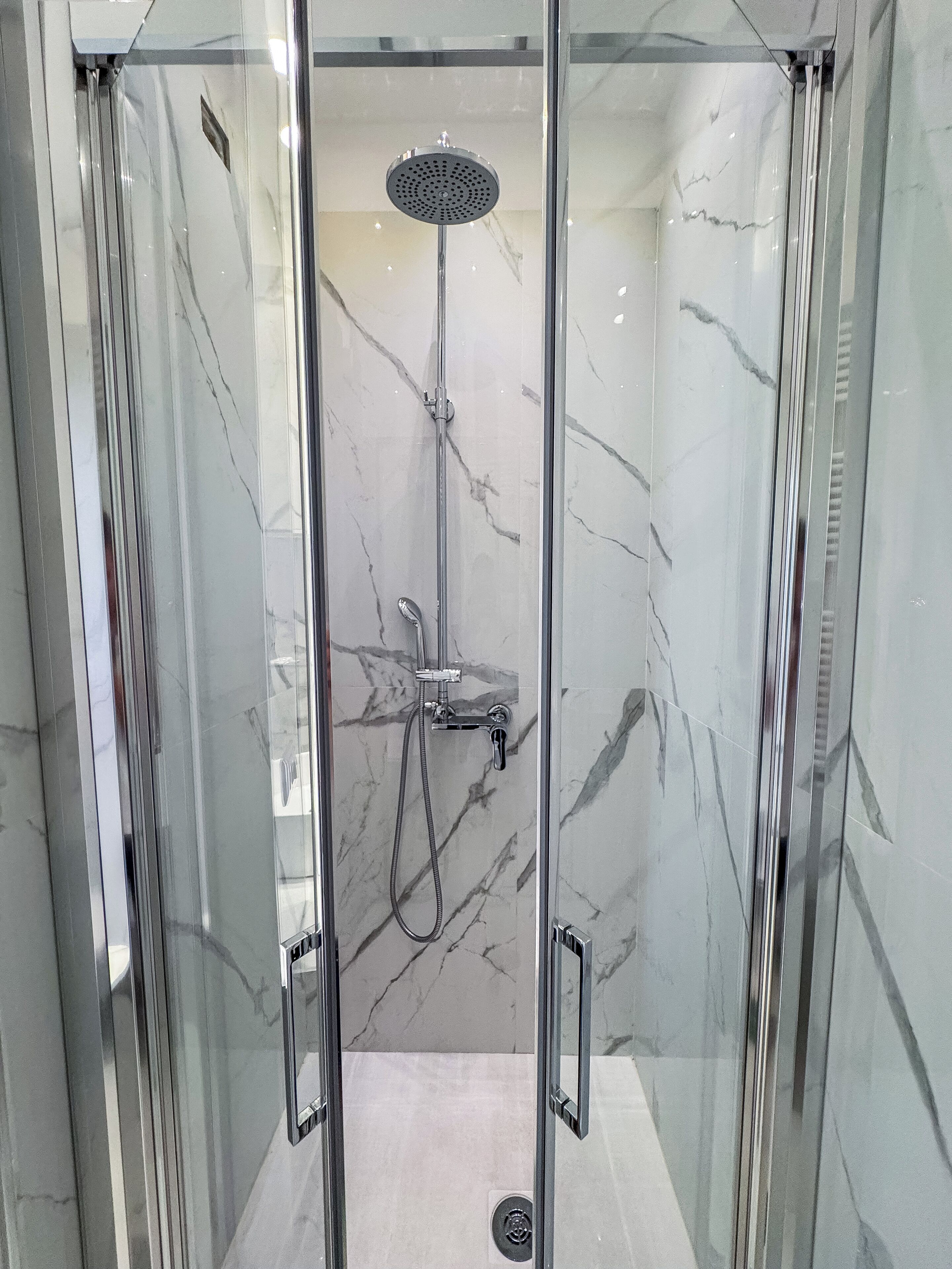 Une douche fermée par des parois en verre, dotée d’un pommeau de douche à main et d’un robinet à main.