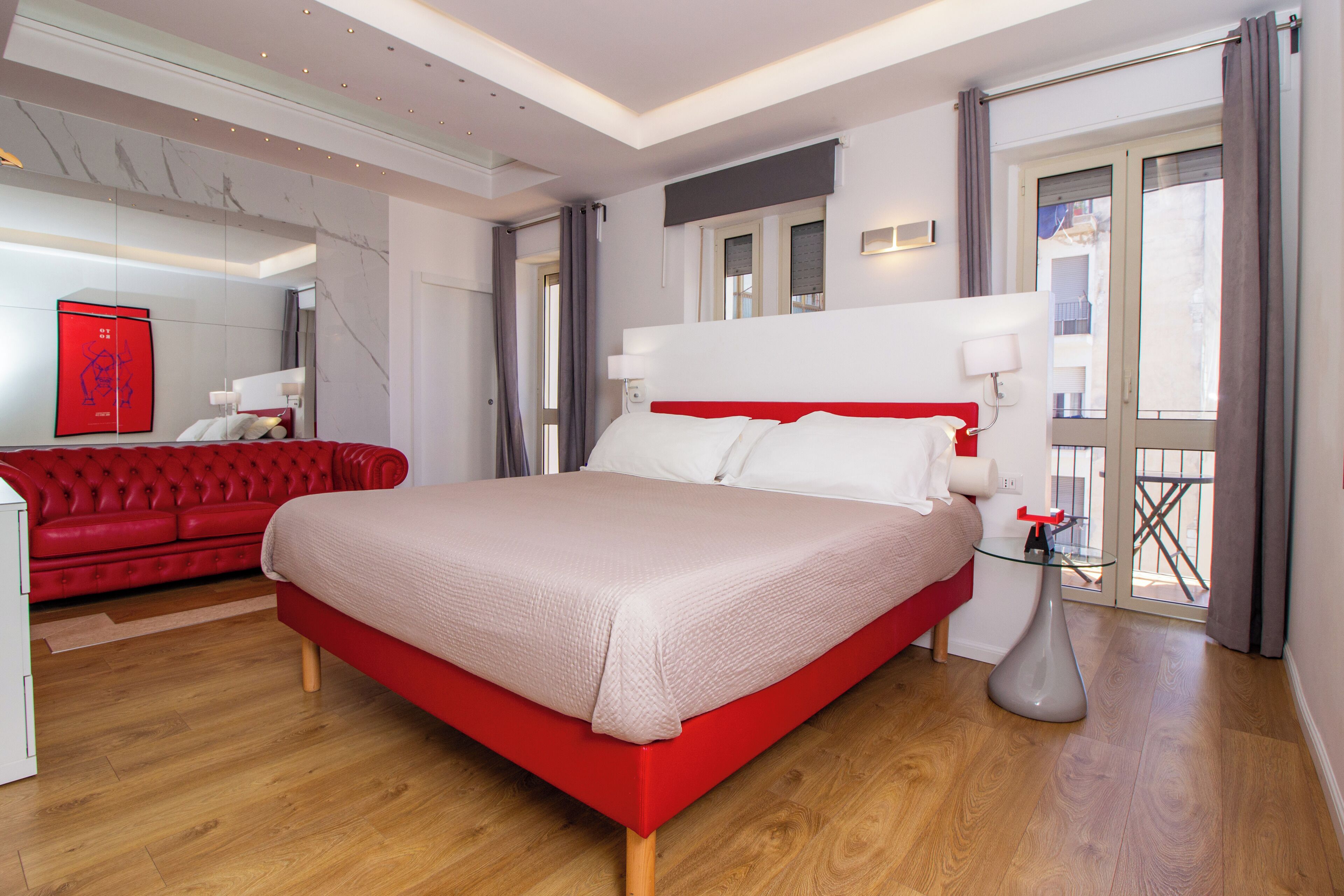 Una camera d'albergo moderna con un letto rosso, pavimento in legno, un divano rosso e un tavolo in vetro.