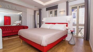 Une chambre d’hôtel moderne avec un lit rouge, un plancher en bois, un canapé rouge et une table en verre.