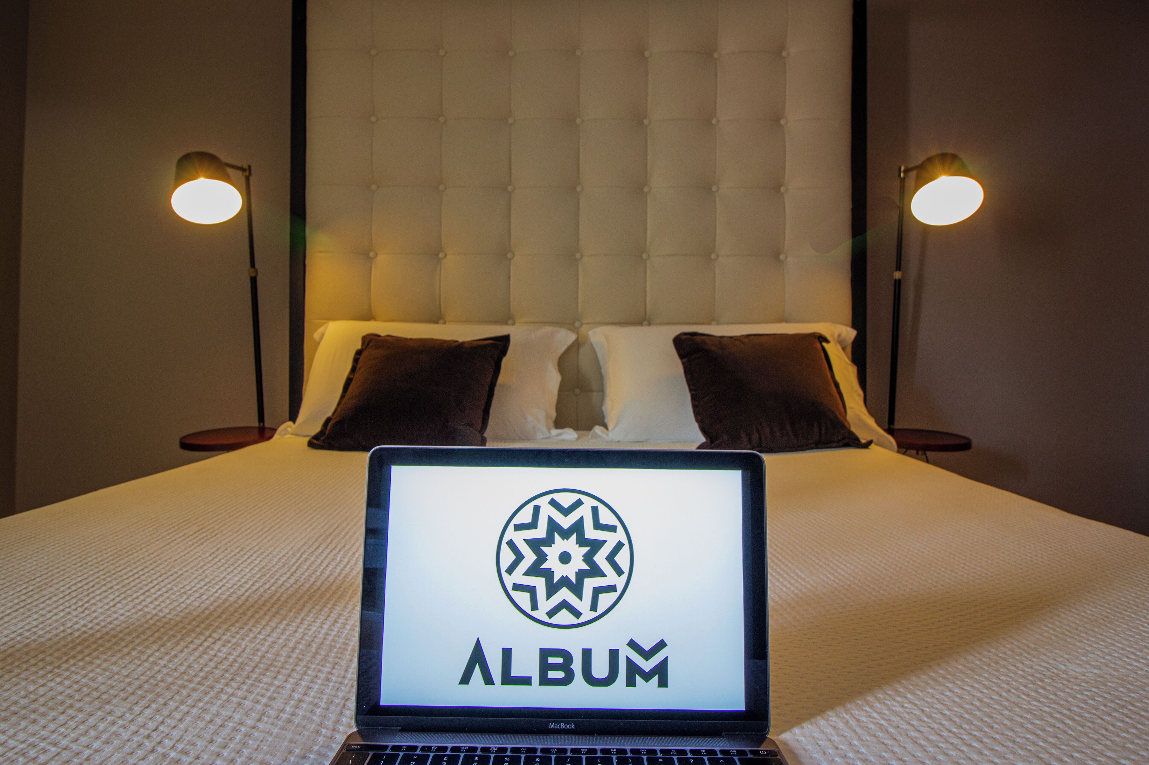Un letto con un laptop che mostra la parola 'ALBUM' in una camera d'albergo.