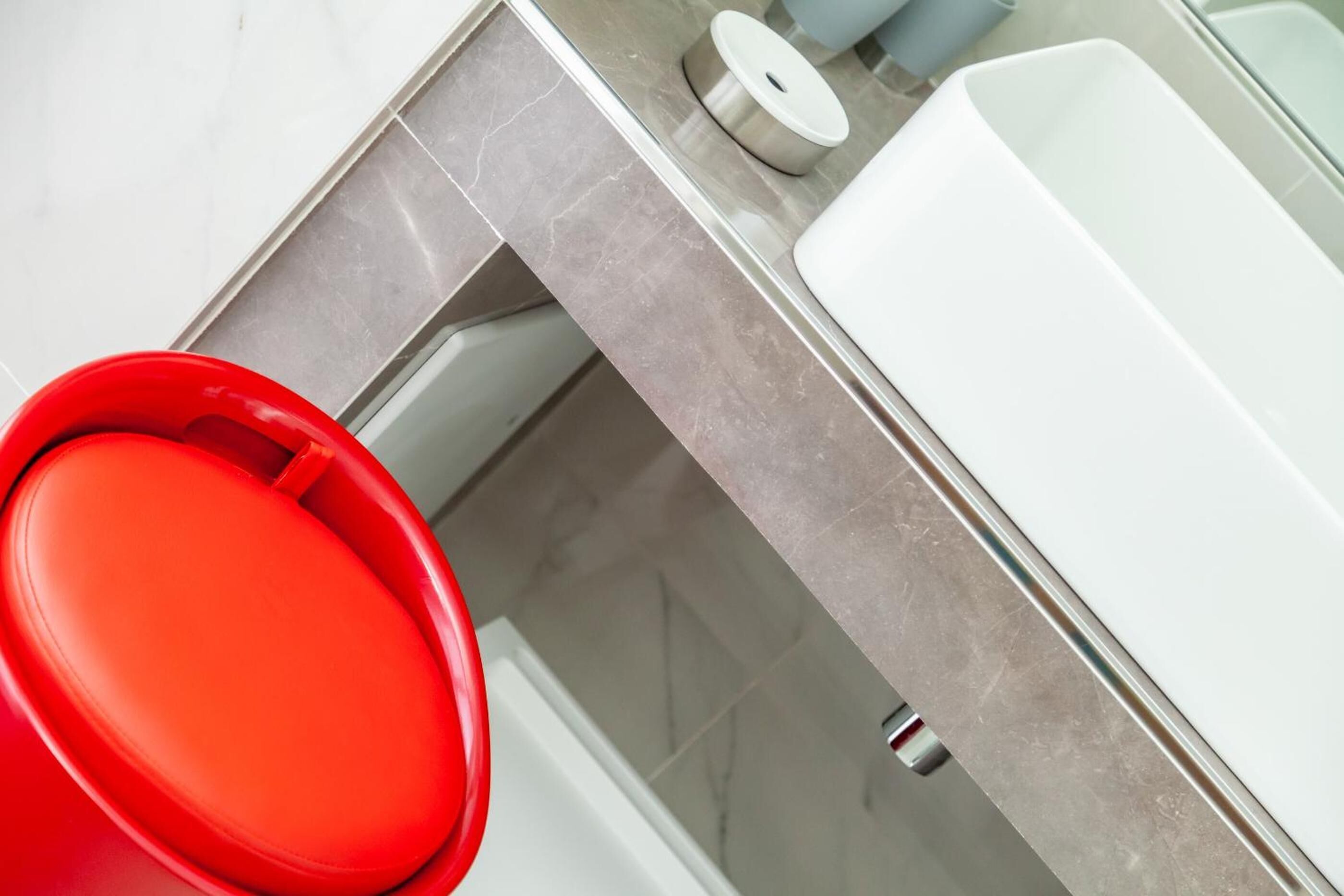 Une salle de bain moderne avec une baignoire rouge, un lavabo blanc et un comptoir en marbre.