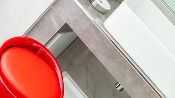Une salle de bain moderne avec une baignoire rouge, un lavabo blanc et un comptoir en marbre.
