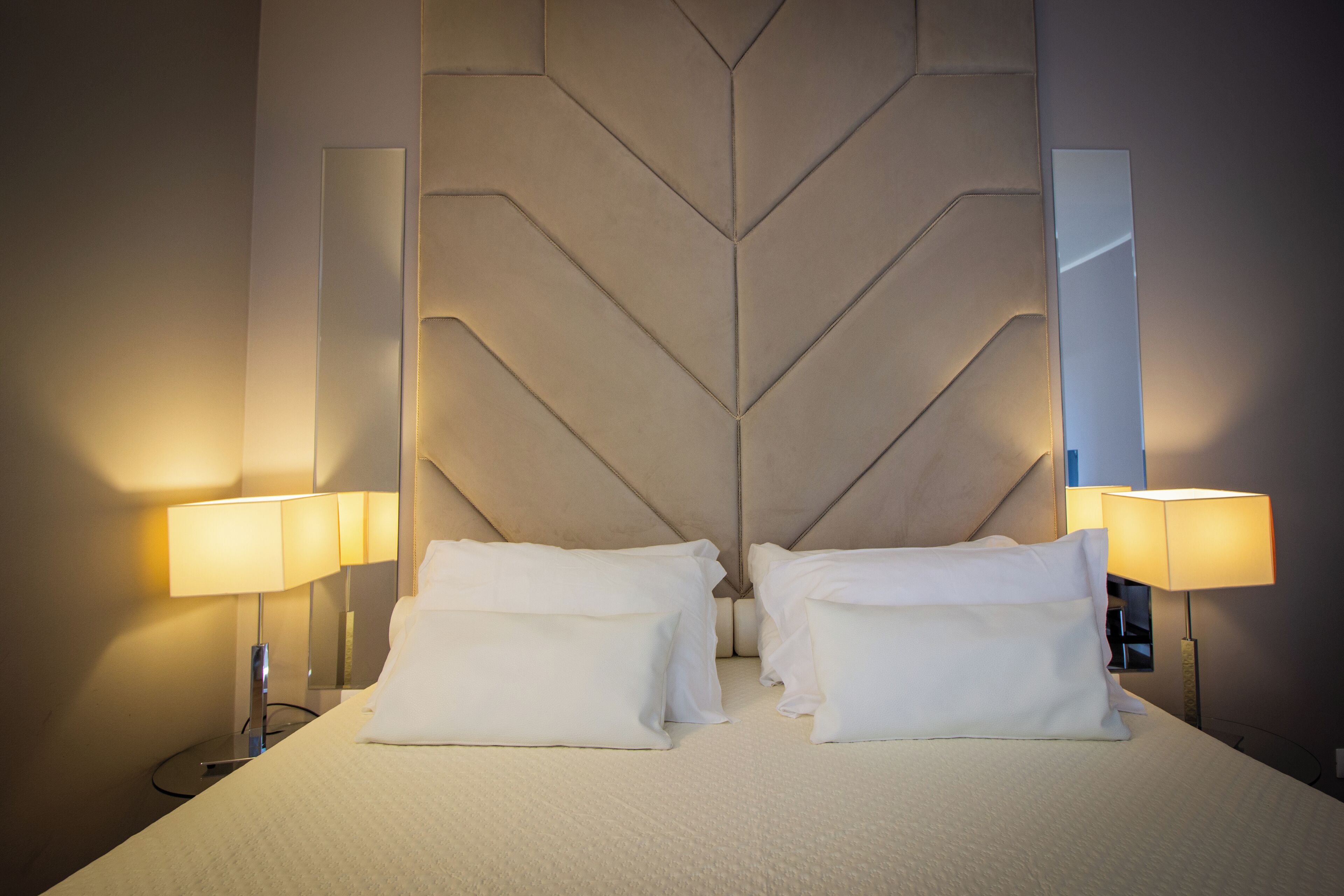 Una habitación de hotel con una cama grande, dos lámparas de noche y un cabecero moderno.