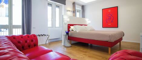 A modern bedroom with a red bed, a red sofa, and a large window with curtains.