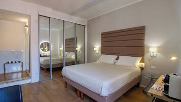 Quarto de hotel com uma cama grande, uma escrivaninha com telefone, um espelho e um painel de vidro.