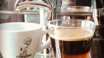 Uma máquina de café servindo café em uma taça de vidro e uma caneca branca.