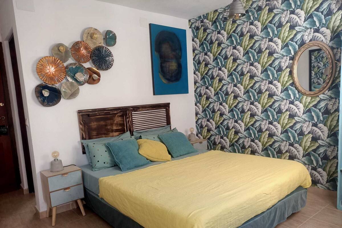 Quarto com cama, mesa de cabeceira, espelho e decorações nas paredes.