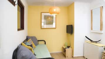 Quarto pequeno e luminoso com uma cama, mesa de cabeceira, luminária e um quadro na parede.